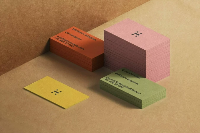 Stacks of pastel business cards on a light brown surface, featuring company contact information and a simple, modern logo design.