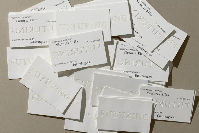 Stack of white business cards with embossed text on gray background, featuring the name 'Victoria Ellis' and the company name 'Futuring'.