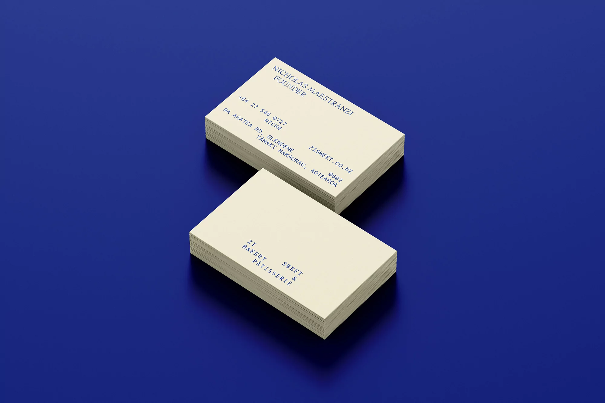 Stacks of cream-colored business cards with dark blue text on a royal blue background, creating a minimalist and professional presentation.