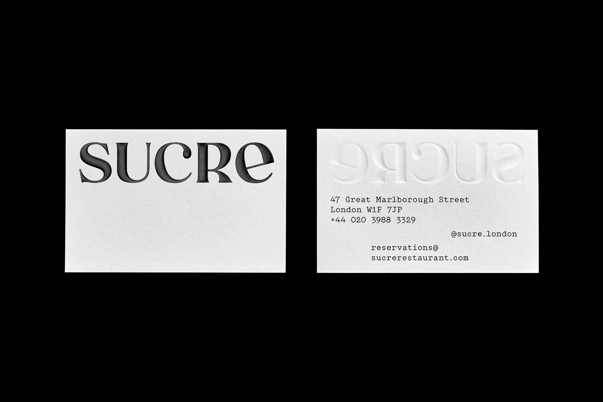 Two white business cards showing debossed typography of the name Sucre against a solid black background.