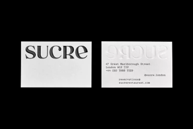 Two white business cards showing debossed typography of the name Sucre against a solid black background.