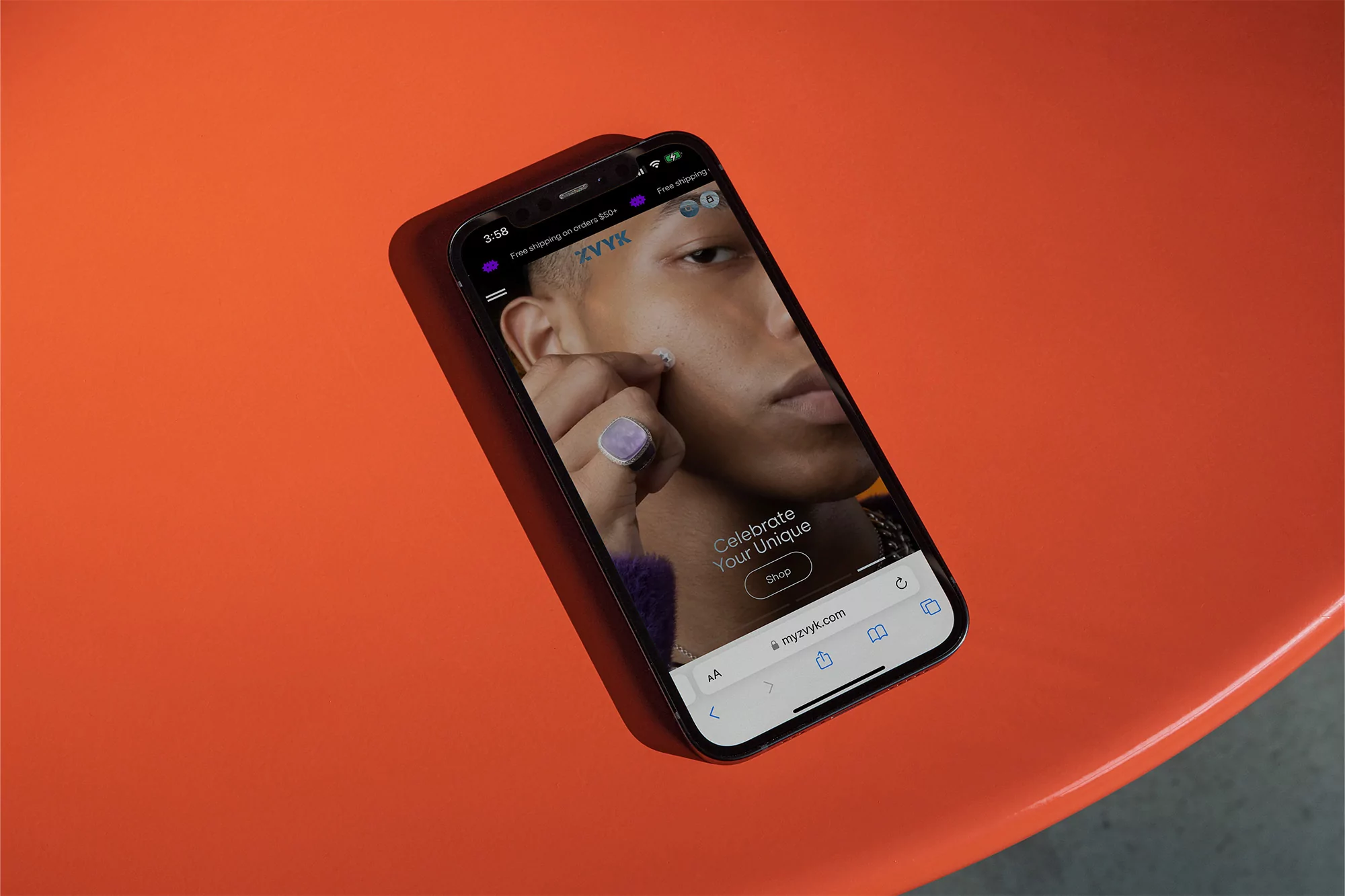 Close-up of a black smartphone displaying the myvzyk.com e-commerce website with a model wearing a ring, on an orange surface.