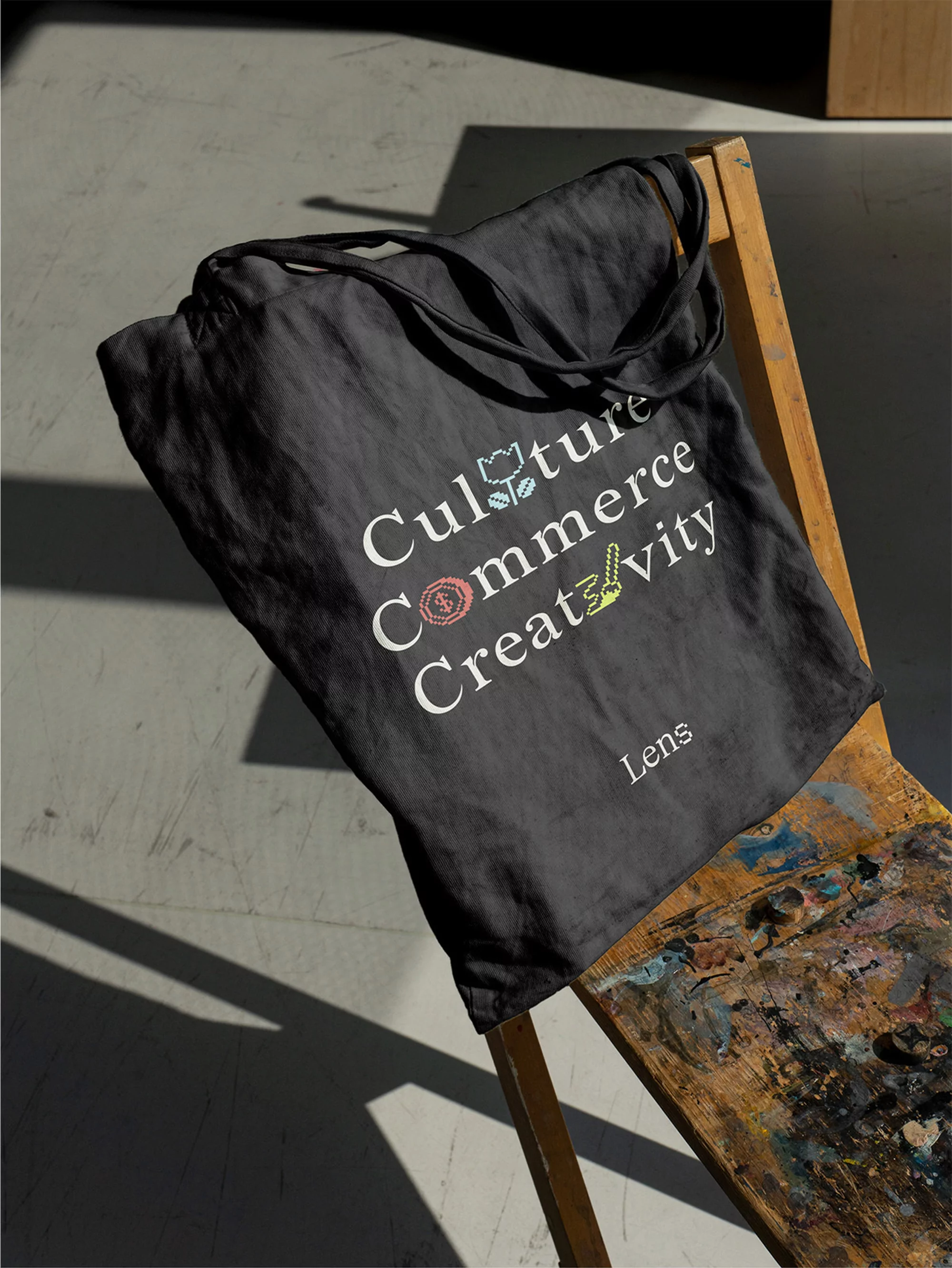 Black tote bag with graphic text on a distressed wood chair, bathed in natural light casting shadows on a concrete floor.