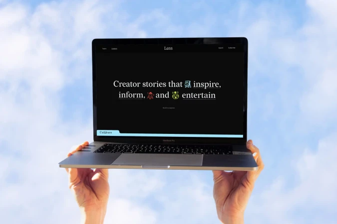 Laptop screen displays 'Creator stories that inspire, inform, and entertain,' held by two hands against a blue sky with clouds.