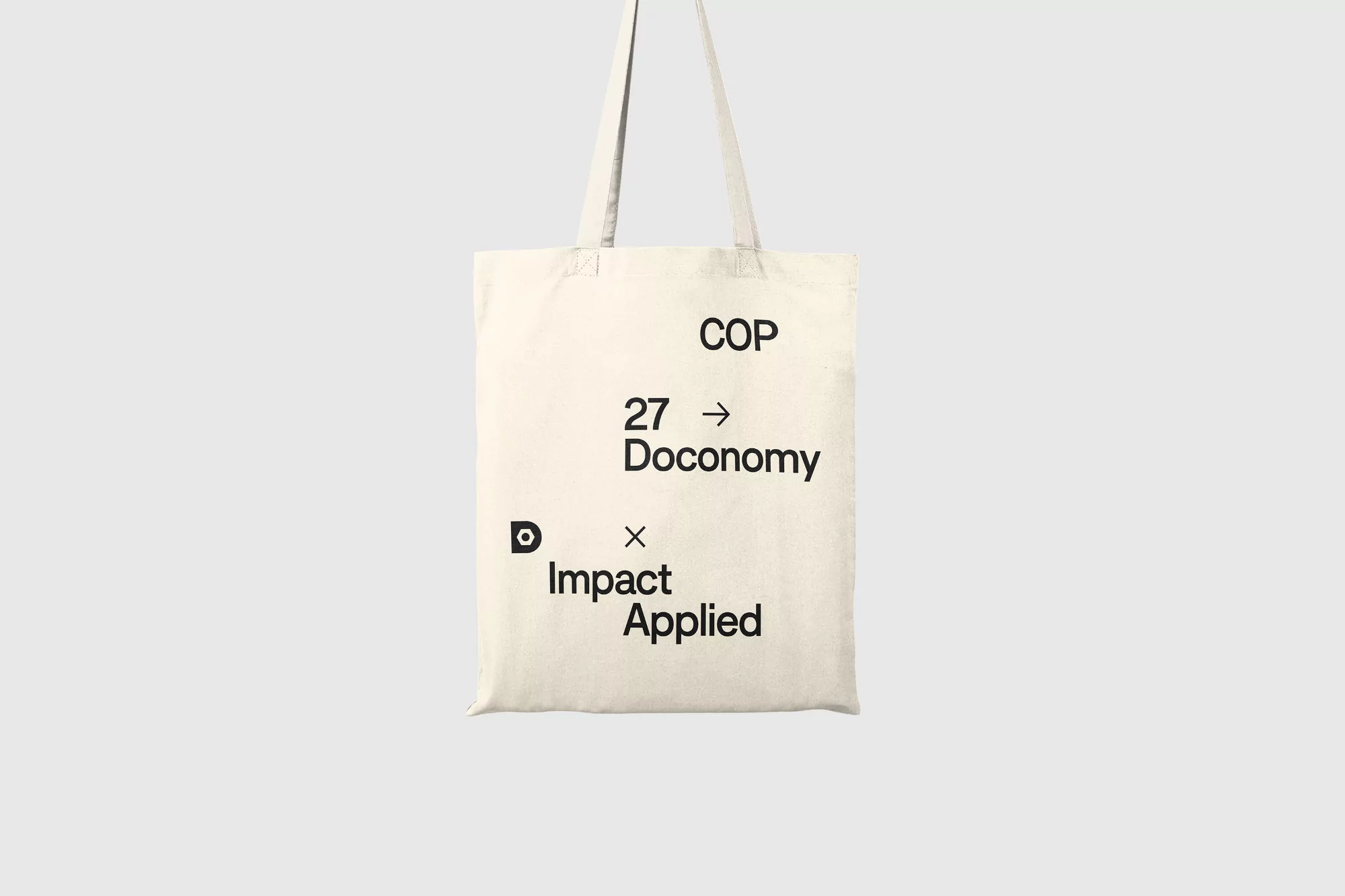 Off-white canvas tote bag featuring black typography centered against a clean grey studio background.