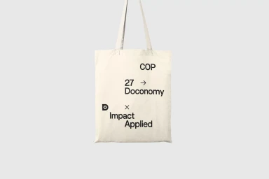 Off-white canvas tote bag featuring black typography centered against a clean grey studio background.