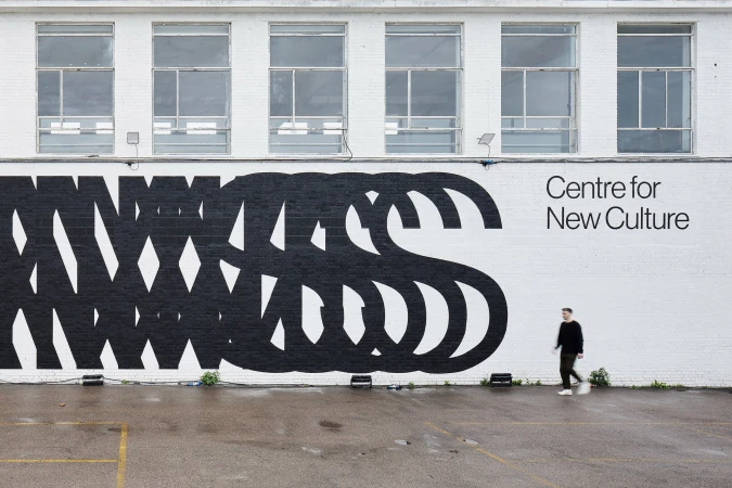 Exterior shot of a building with a black and white mural and an adult male walking on a wet asphalt surface.