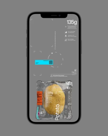 A single potato sealed in clear plastic packaging is displayed on a grey smartphone screen, presented against a solid grey backdrop.