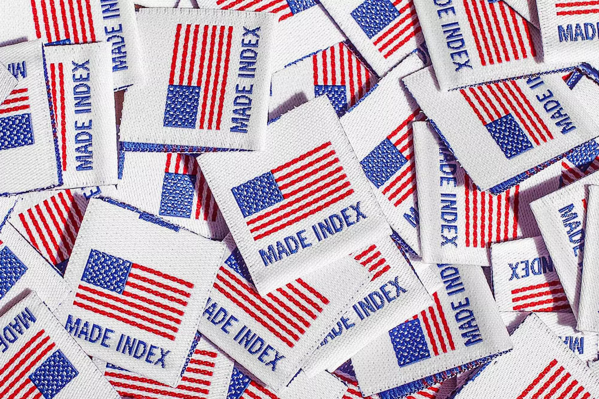 Close-up of many white fabric labels with red stripes and blue stars, repeating the text 'MADE INDEX' in blue font.