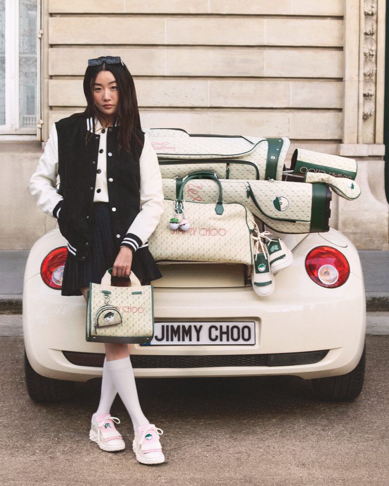 A fashionable Asian woman stands near a white car filled with golf equipment, showcasing a handbag, in an outdoor, urban setting.