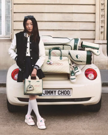 A fashionable Asian woman stands near a white car filled with golf equipment, showcasing a handbag, in an outdoor, urban setting.