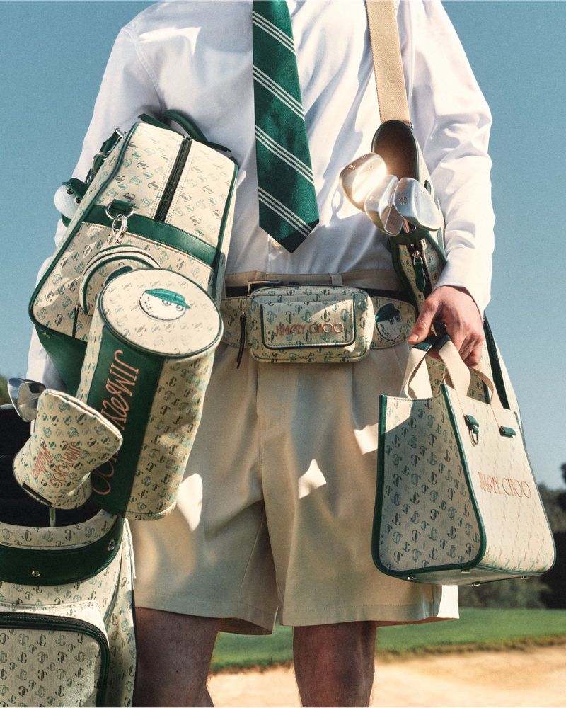 A man in golf attire, including a shirt, shorts, and tie, is carrying several patterned golf bags and a tote bag in an outdoor setting.
