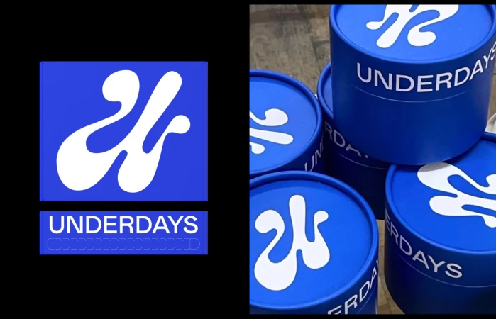 Eye-level studio shot of blue cylindrical boxes stacked with white logos and 'UNDERDAYS' text against a stark black backdrop on the left.