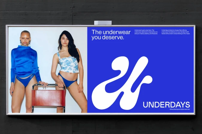 Two female models posing next to a red stool in front of a white wall, alongside a blue billboard featuring white typography for Underdays.
