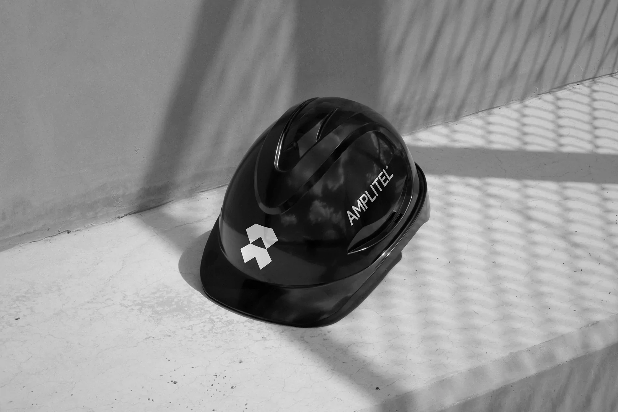 Elevated eye-level studio shot of a black hard hat with the Amplittel logo on a grey surface, capturing shadows and industrial safety.