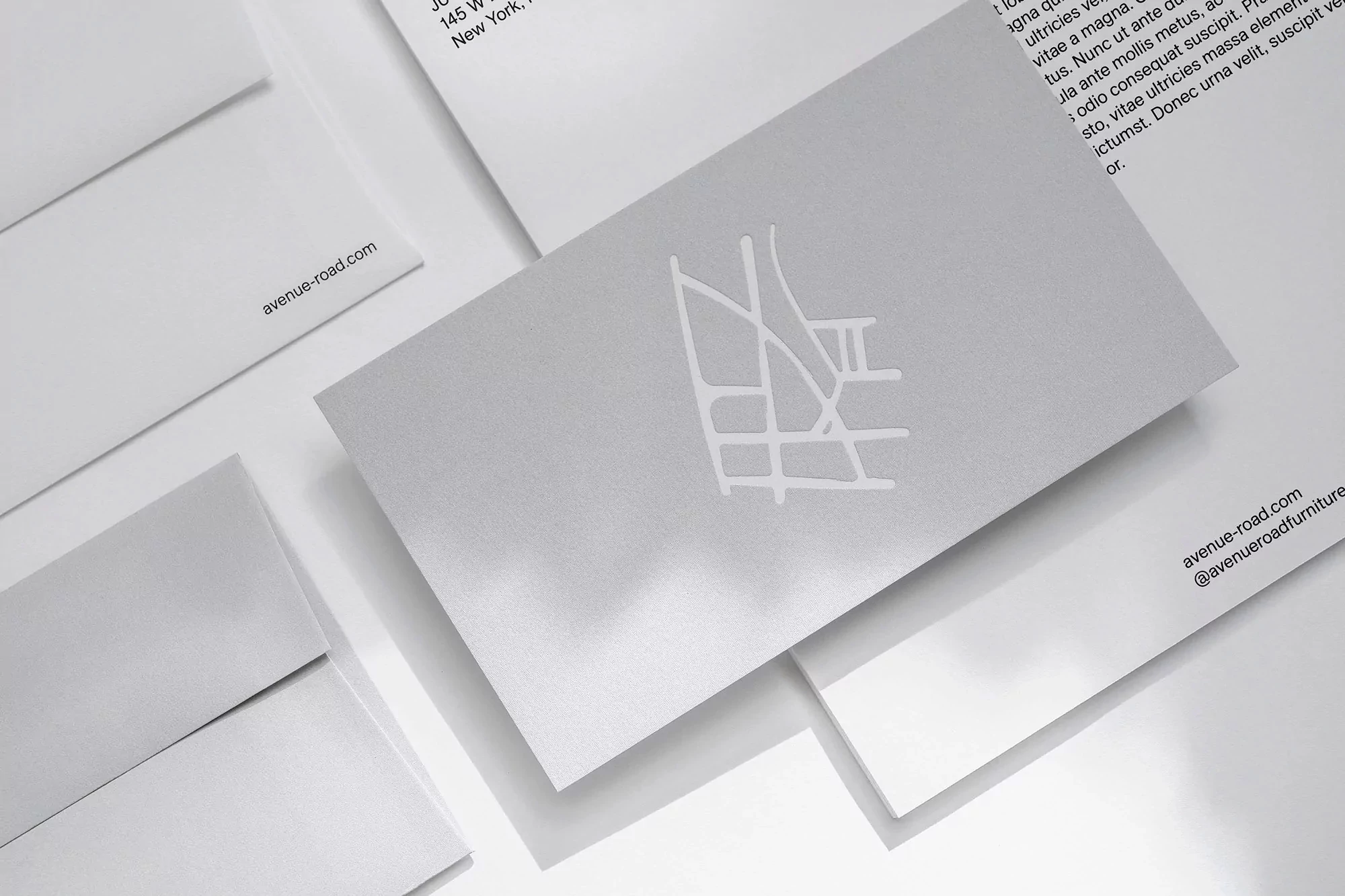 Close-up of silver and white business cards and envelopes with minimal design, set on a white surface in bright, even lighting.