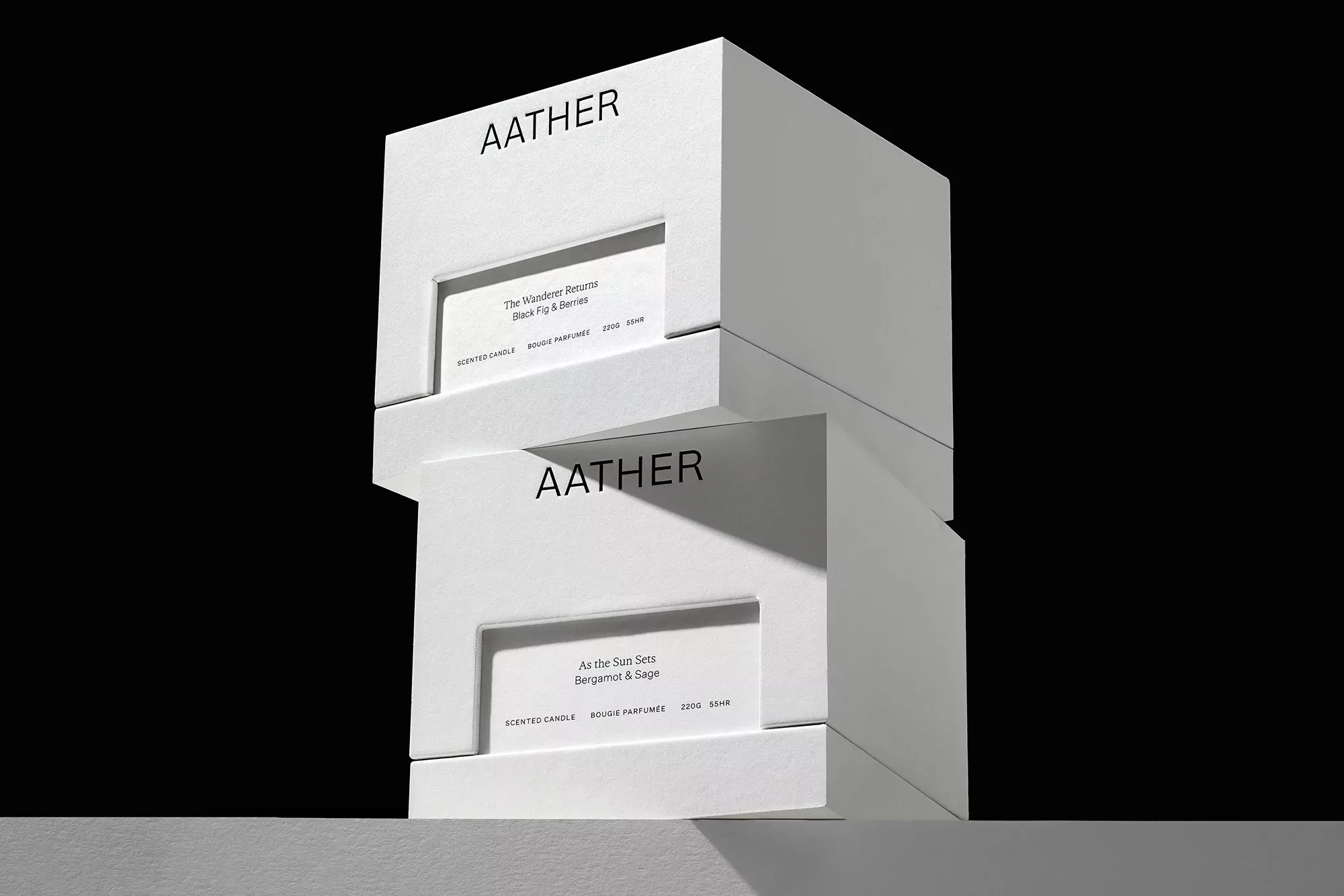 Two white AATHER candle boxes stacked against a black background, showing product names 'The Wanderer Resurr' and 'As the Sue Sets'.