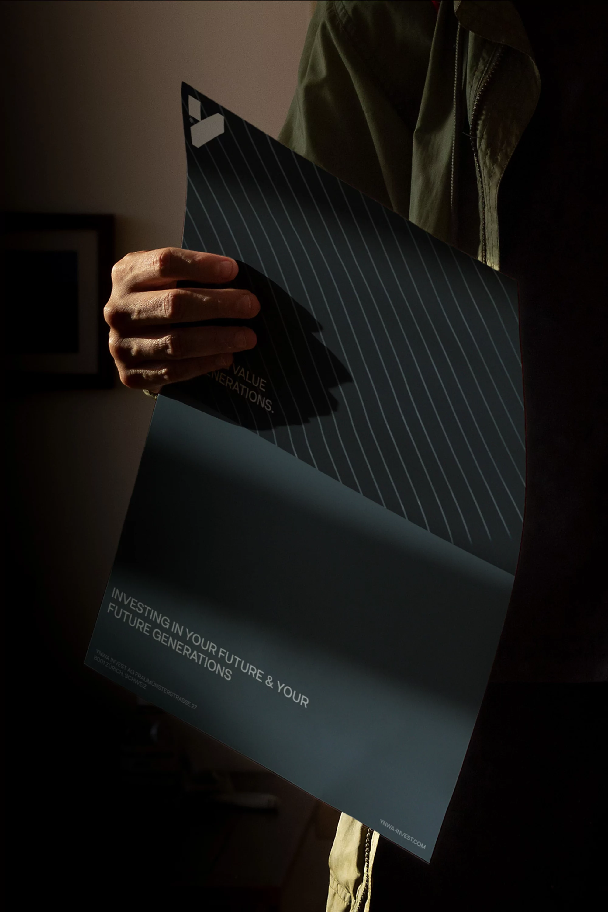 Adult holding a black and white pinstripe brochure with text, indoors in dim light, wearing a green long-sleeve shirt or jacket.