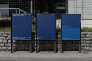 Three vertical blue display panels with white text and line patterns mounted in metal stands outdoors against a stone wall.