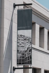 Vertical dark banner signage hanging from a classical stone building exterior with architectural detail