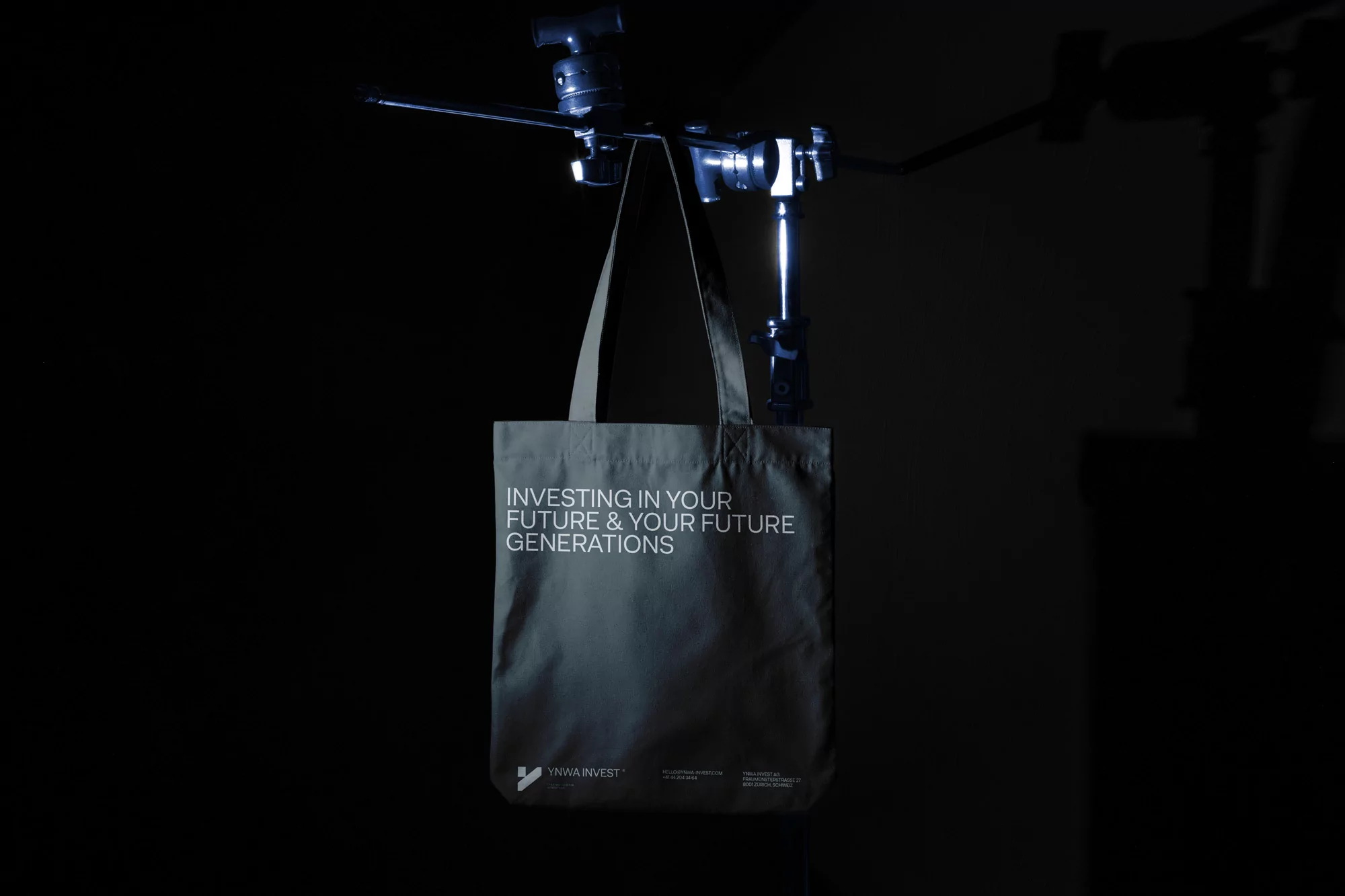 Olive green tote bag hanging from a studio light stand against a dark background