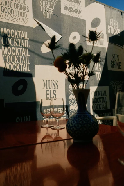 Still life of wine glasses, vase with thistles, and an orange fruit set on a red table, with a graffiti wall as a backdrop.