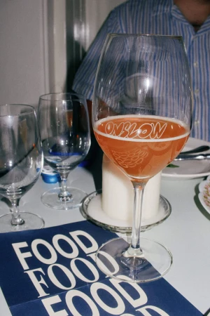 Wine glass filled with pink beverage on table with food menu and other glasses, set in an indoor dining environment.
