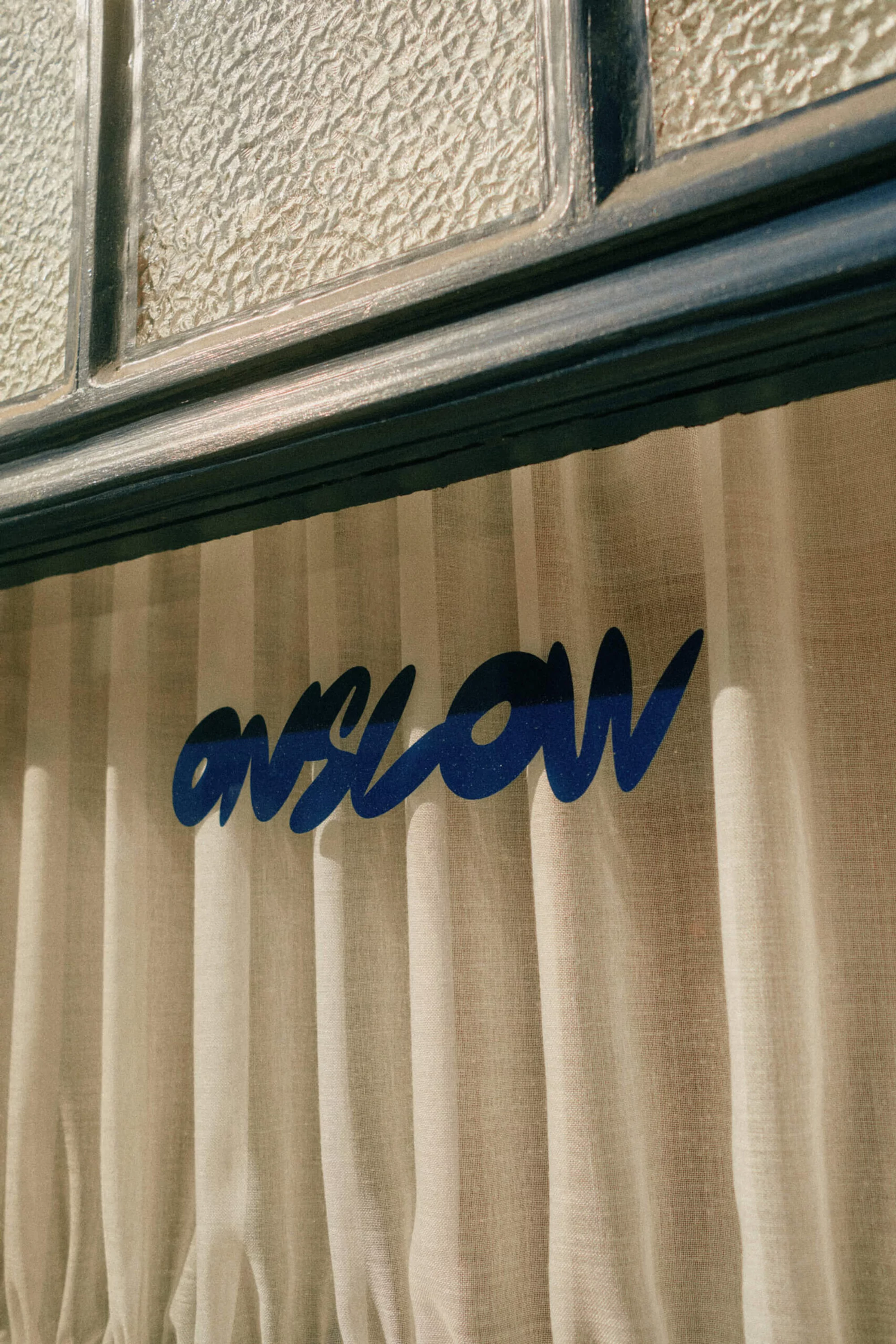 Close-up of a window with textured glass and a curtain with the word 'onslow' printed on it in blue ink.