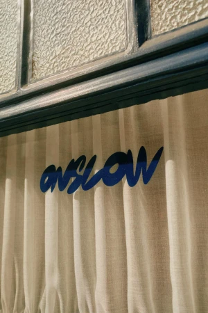 Close-up of a window with textured glass and a curtain with the word 'onslow' printed on it in blue ink.