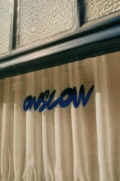 Blue typography reading Onslow displayed across sheer pleated fabric curtains below a dark window frame.