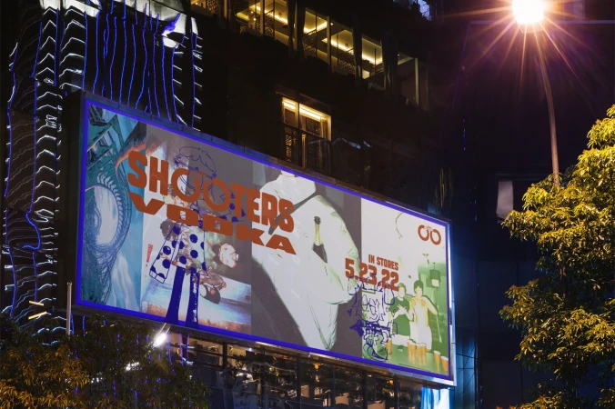Nighttime view of a Shooters Vodka advertisement on a building in an urban environment, illuminated by a street lamp.