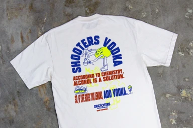 White graphic t-shirt featuring bold blue typography and yellow lemon illustration on the back laid on stone