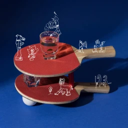 Two stacked red ping pong paddles holding shot glasses with whimsical white hand-drawn doodle characters against a deep blue background.