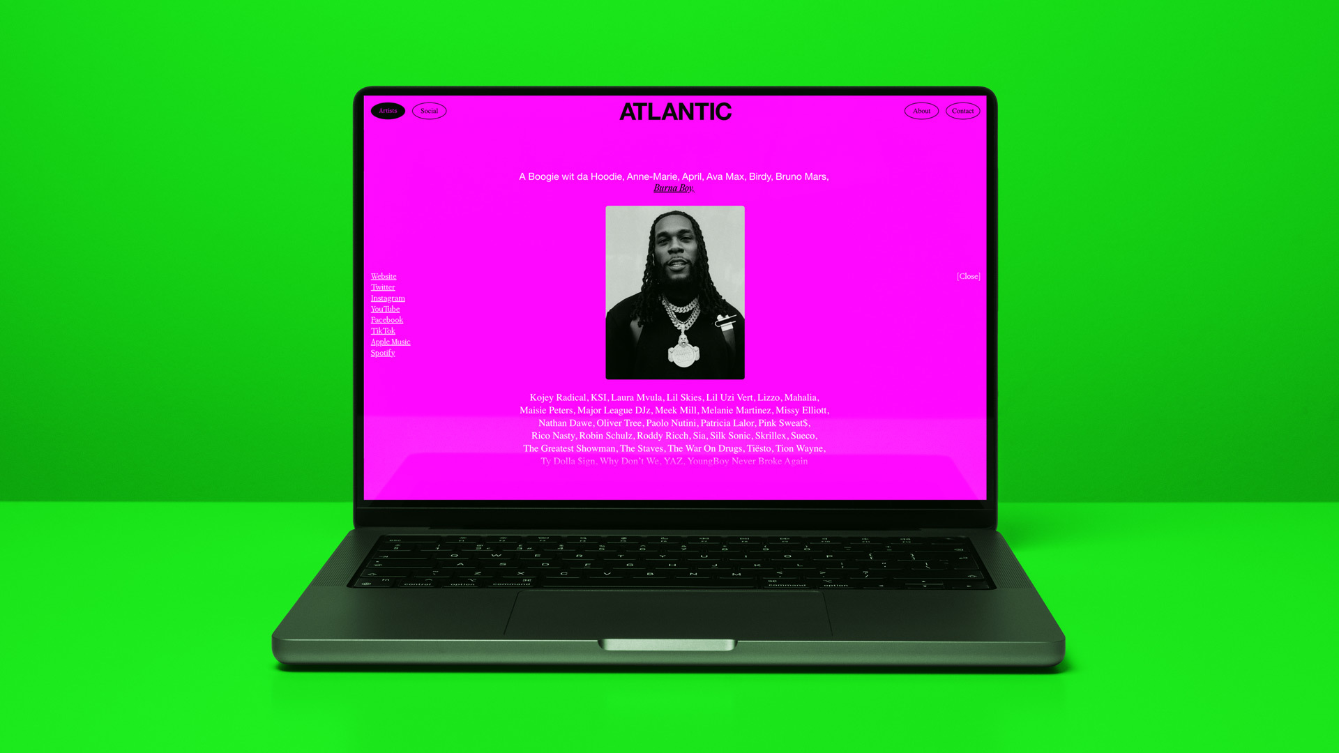 Laptop displays Atlantic Records website with a Burna Boy image on a bright green background, showcasing music industry content.