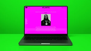 A laptop displaying the Atlantic Records UK website featuring bold pink background and artist listings against a solid green surface.