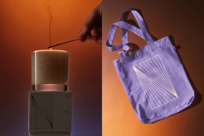 Still life of a lit candle on a box next to a lavender tote bag against an orange gradient background, showcasing product branding.
