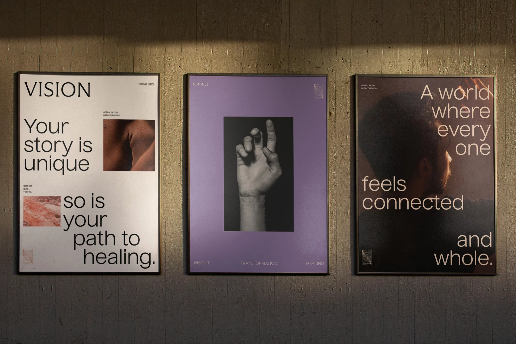 Three framed posters with text and abstract imagery hang on a textured gray wall, illuminated by a soft, diffused light source.