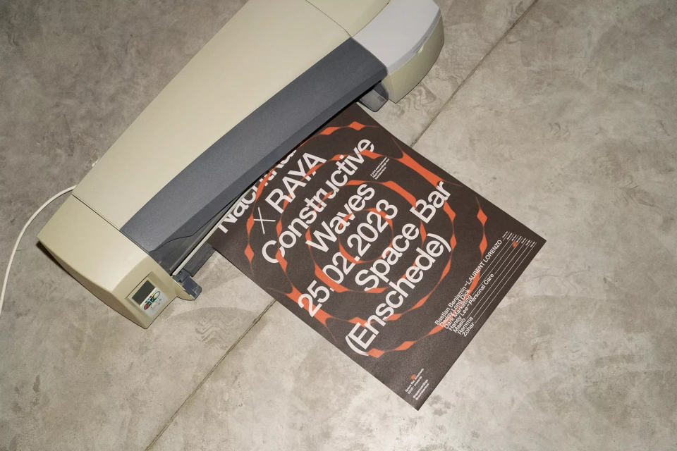 Poster being laminated. Text reads 'Constructive Waves Space Bar 25.02.2023 (Enschede)'. Tan and gray laminator on gray surface.