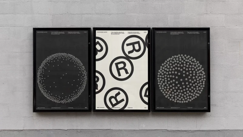 Three black-framed posters hang on a concrete wall. The posters showcase graphic designs featuring dots and the letter R within circles.