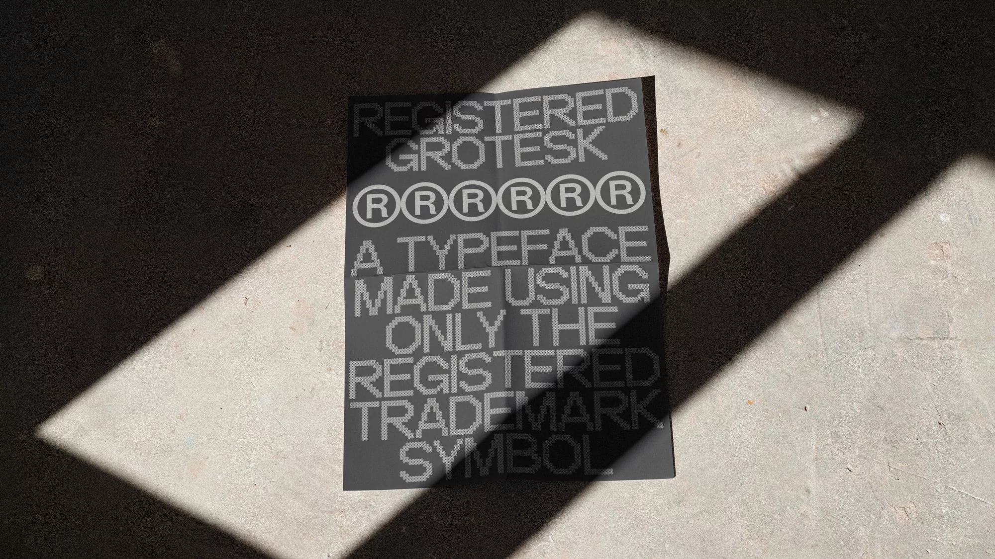 A gray poster with text using only the registered trademark symbol sits on a concrete surface with shadows creating a geometric pattern.