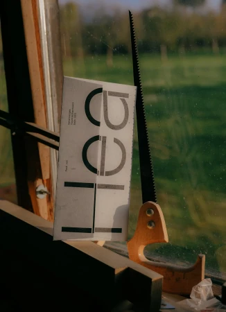 Still life photograph capturing a book, hand saw, and carpentry elements in a naturally lit, cluttered environment. Wood and printed text visible.