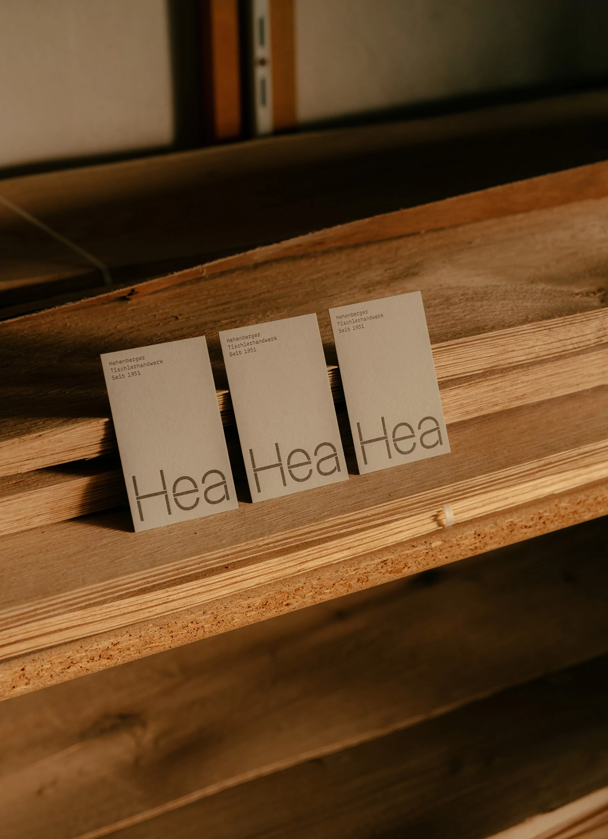 Three branded business cards with the name Hea resting on a wooden shelf