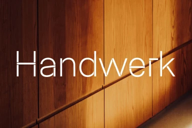 White stylized typography reading Handwerk superimposed over a polished warm wood paneled wall.