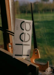 Printed paper branding envelope for Hea resting next to a hand saw against a windowsill with a green outdoor background.