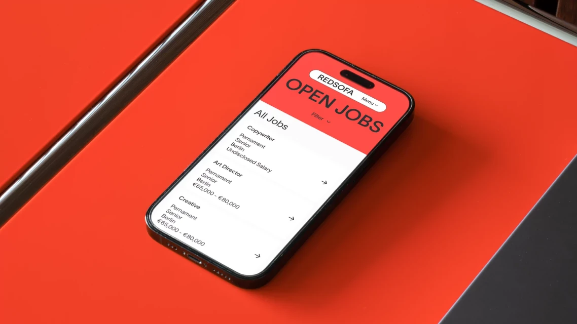 Smartphone displaying a job application webpage, prominently featuring listings for Copywriter, Art Director, and Creative roles with a red background.