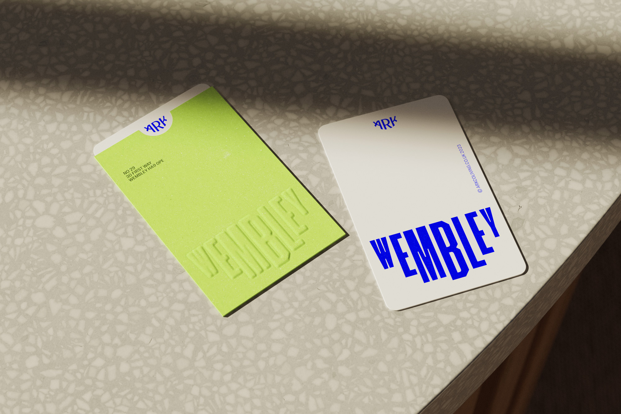Two business cards, one neon green with embossed lettering, one white with blue lettering, both displaying the word Wembley.