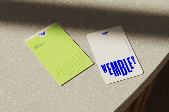 Two business cards, one neon green with embossed lettering, one white with blue lettering, both displaying the word Wembley.