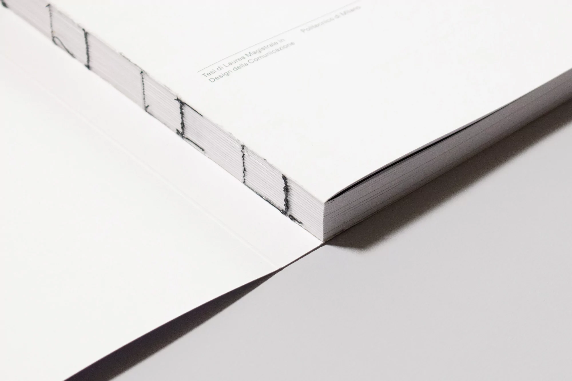 Close-up studio shot of a perfect-bound book with a white cover and visible stitching, emphasizing its texture and minimalist aesthetic.