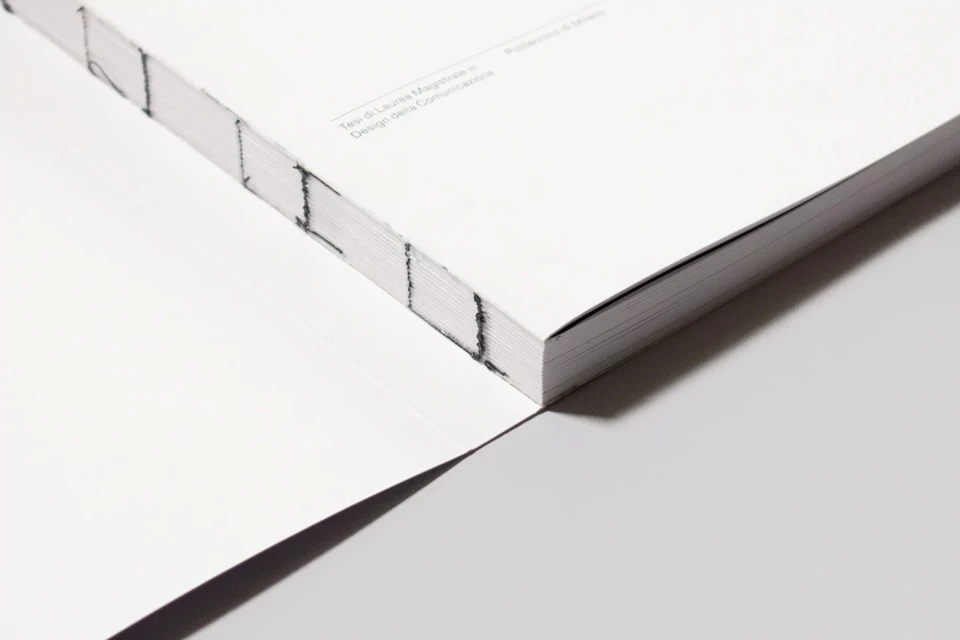 Close-up studio shot of a perfect-bound book with a white cover and visible stitching, emphasizing its texture and minimalist aesthetic.