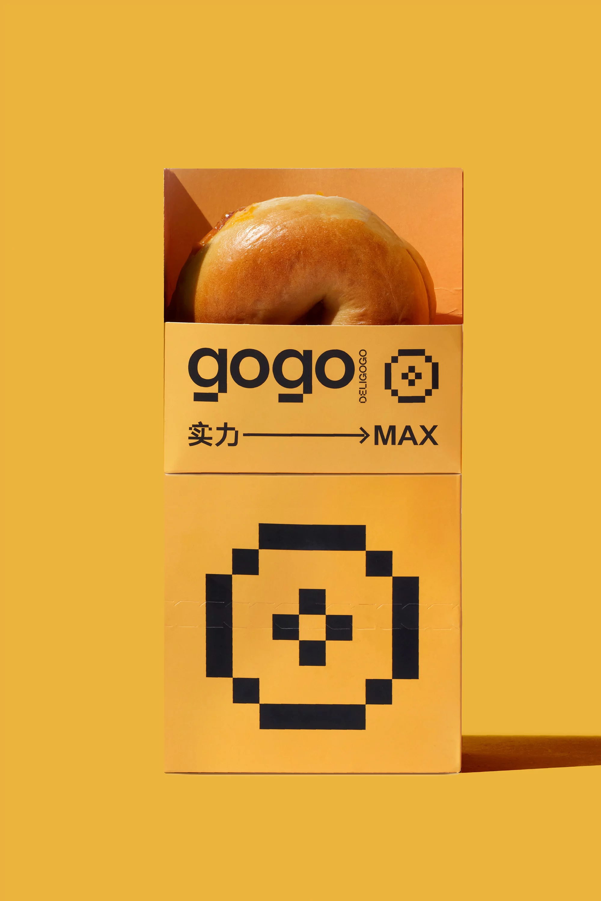 Still life studio shot of a donut inside its yellow branded packaging, featuring geometric pixelated design on a solid yellow backdrop.